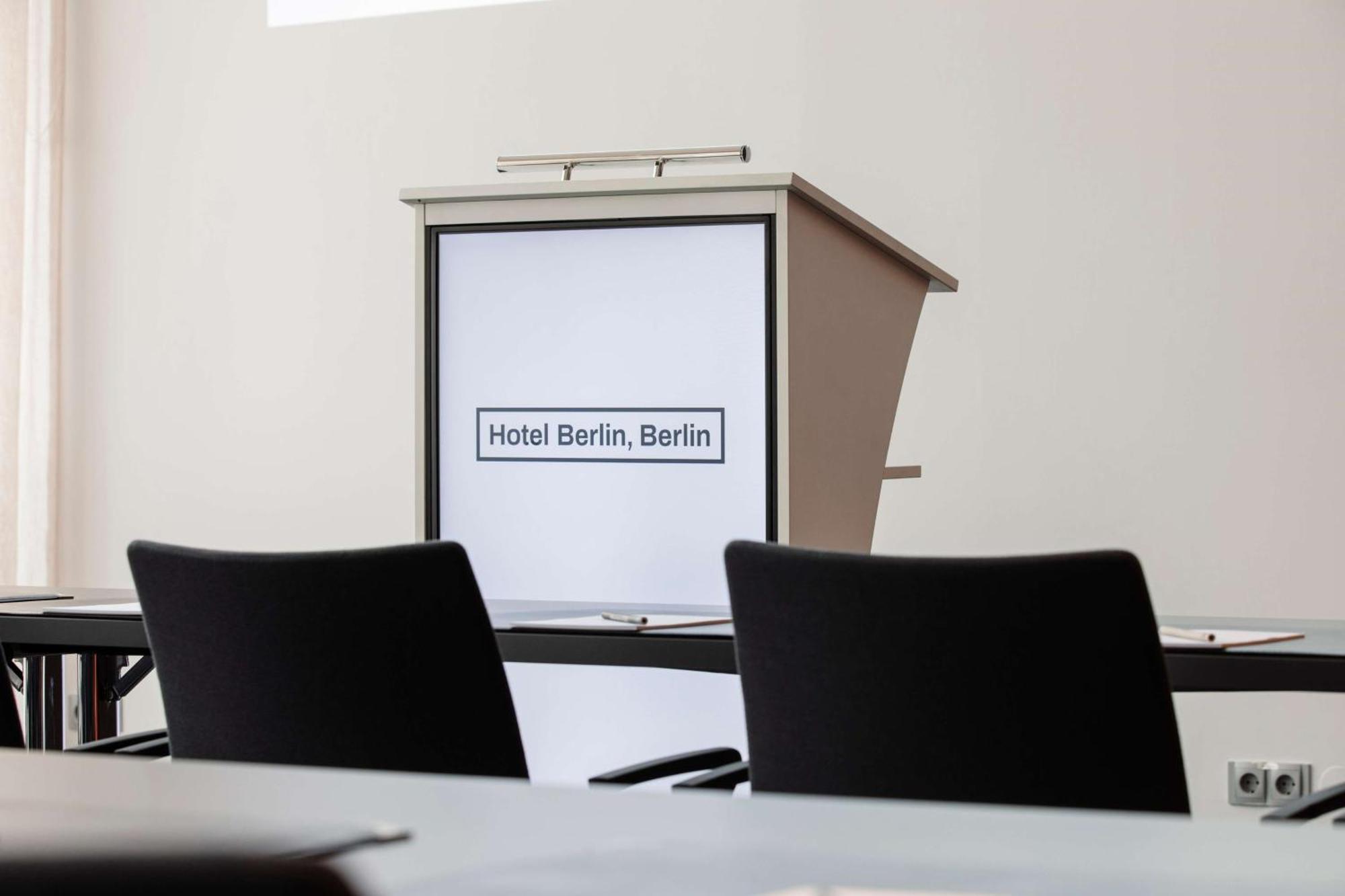 Hotel Berlin, Berlin, A Member Of Radisson Individuals Buitenkant foto The photo shows a conference setup in a room. In the foreground, there are two black chairs facing a grey conference table. At the front, there's a lectern or podium that features a sign reading "Hotel Berlin, Berlin." The background is minimalistic,