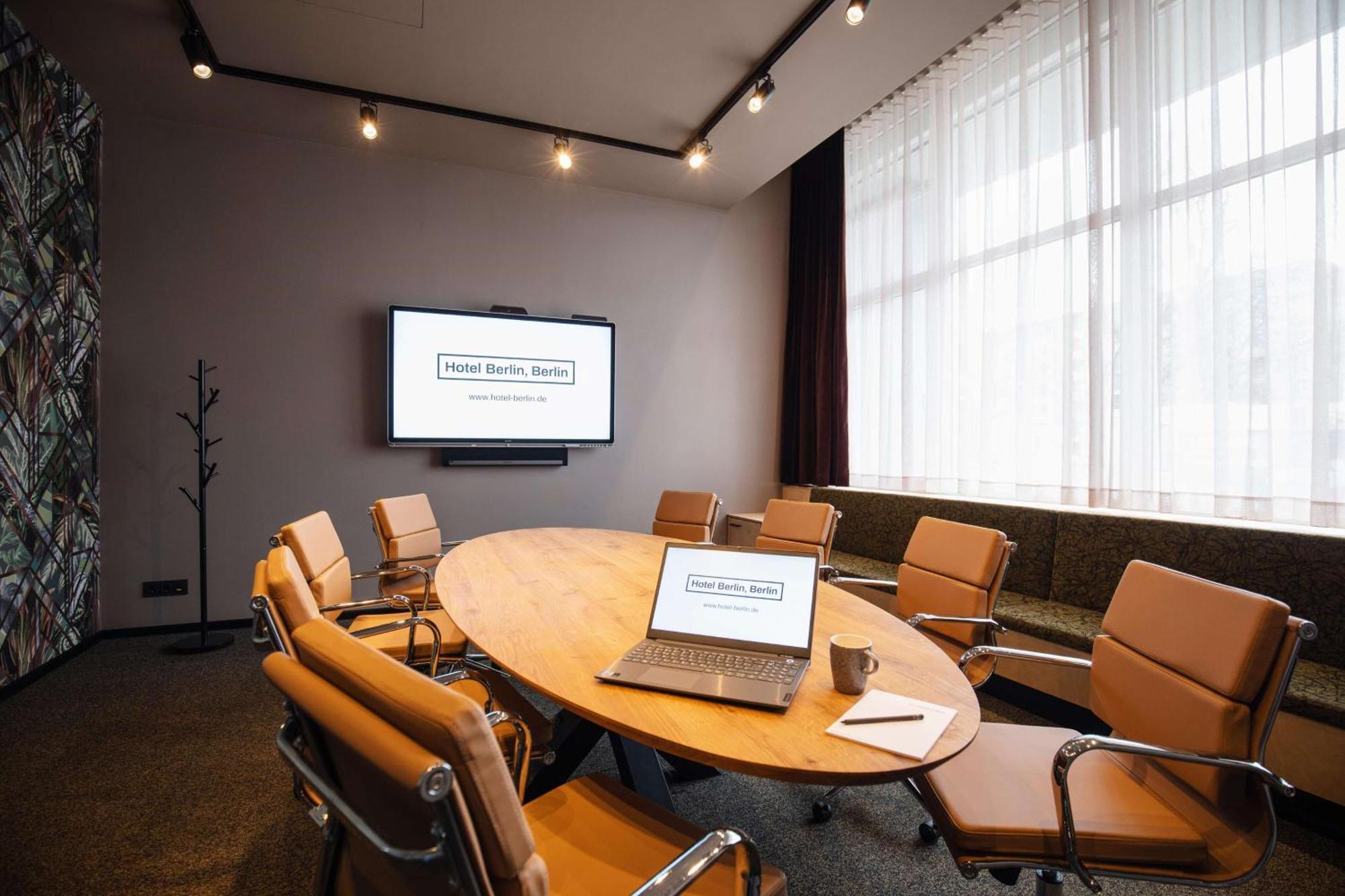 Hotel Berlin, Berlin, A Member Of Radisson Individuals Buitenkant foto The image depicts a modern conference room. It features a large oval table surrounded by several chairs. On the table, there is a laptop open along with a small notepad and a cup, likely indicating preparation for a meeting. A wall-mounted screen dis