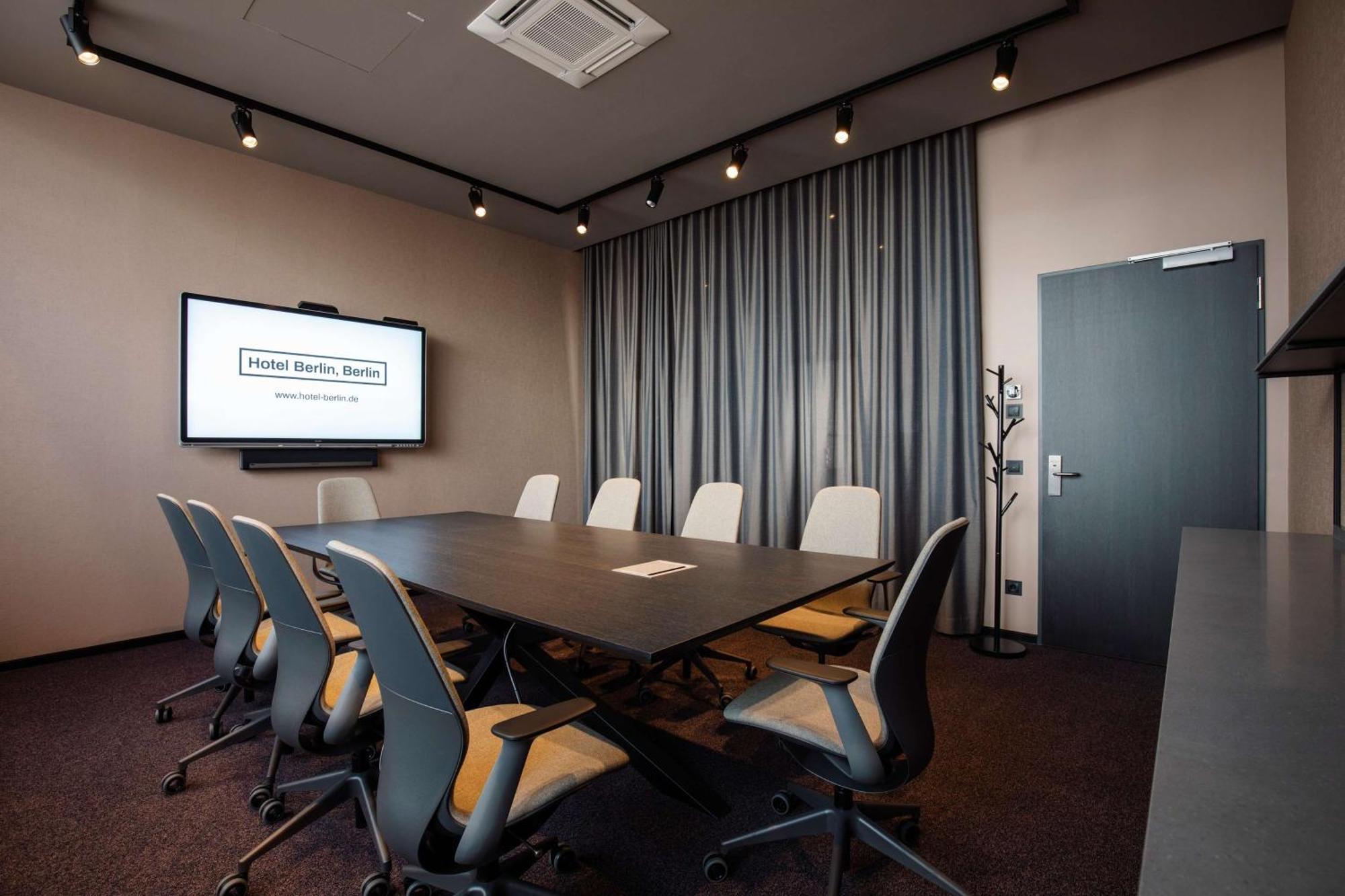 Hotel Berlin, Berlin, A Member Of Radisson Individuals Buitenkant foto The image depicts a modern conference room. In the center, there is a large rectangular table surrounded by several office chairs. On the wall opposite the table, there's a screen displaying a presentation or meeting title. The room features curtains