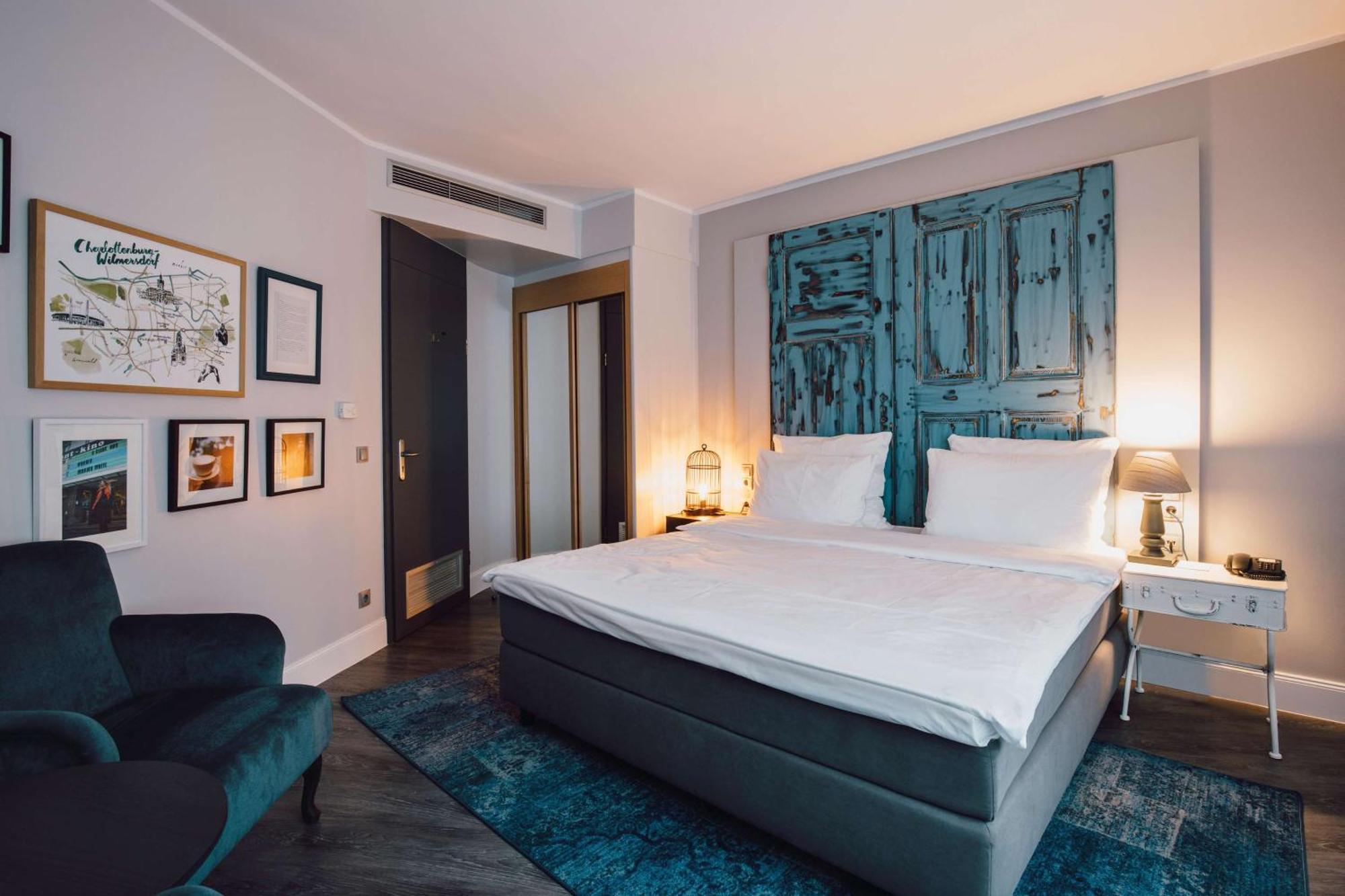 Hotel Berlin, Berlin, A Member Of Radisson Individuals Buitenkant foto The photo shows a modern hotel room with a minimalist design. In the center, there is a large bed with white bedding and two white pillows. Behind the bed, there is a decorative wall featuring a rustic blue panel. To the left, there are framed artwor